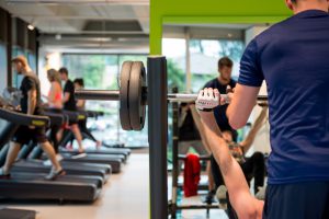 Atleta solleva bilanciere in sala pesi del 4Fit Fitness Club di Carlazzo, con tapis roulant sullo sfondo