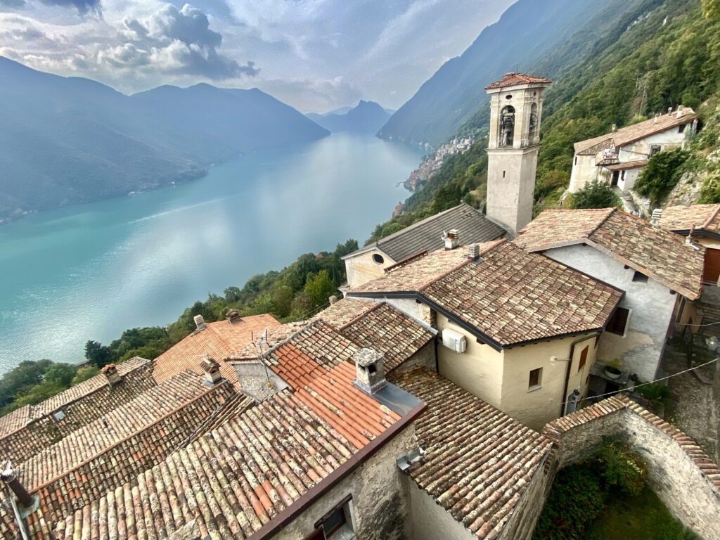 Vista dei tetti del borgo di Castello Valsolda con il campanile e il Lago Ceresio sullo sfondo